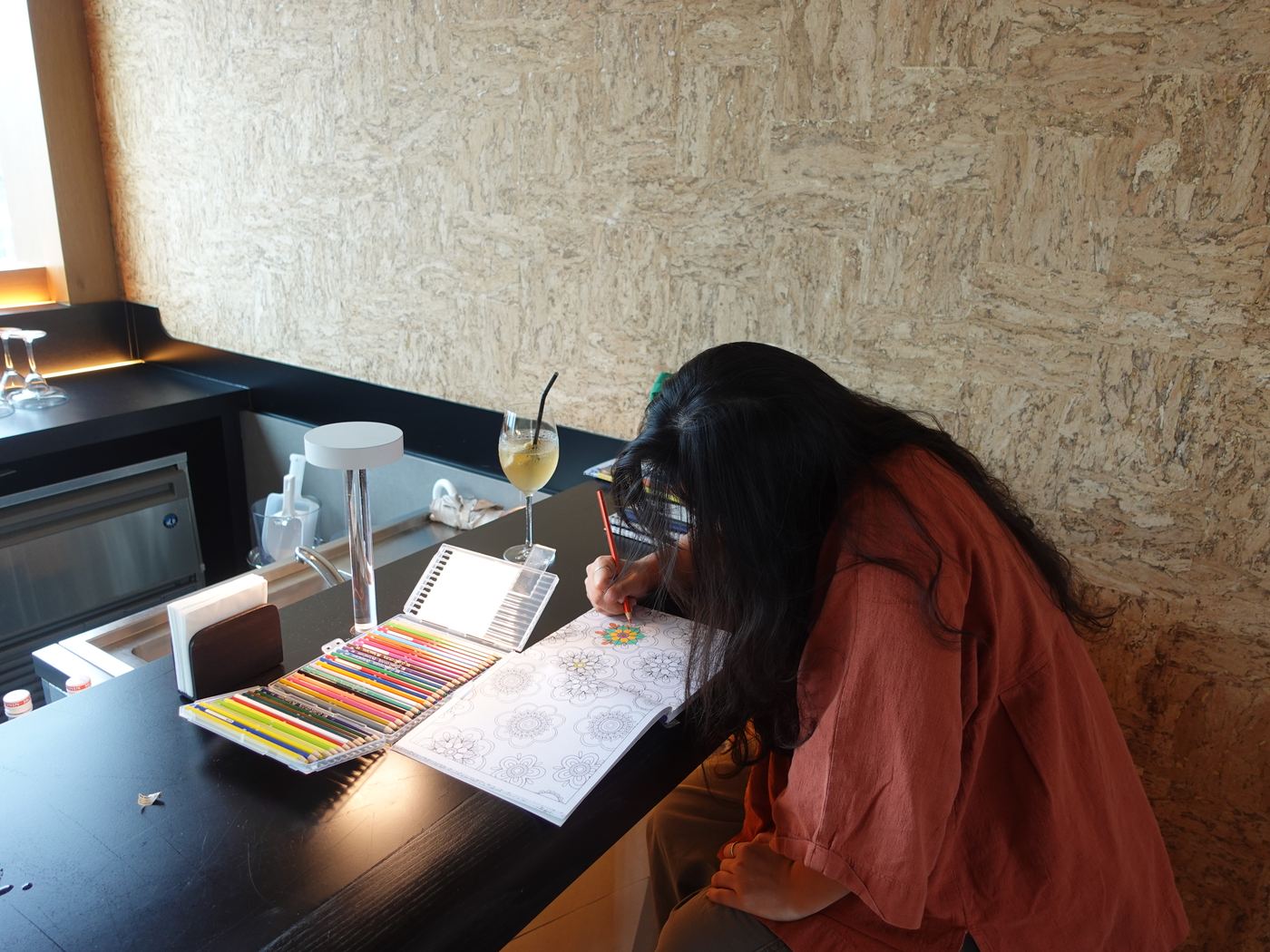 A guest colours a mandala page at the bar with coloured pencils