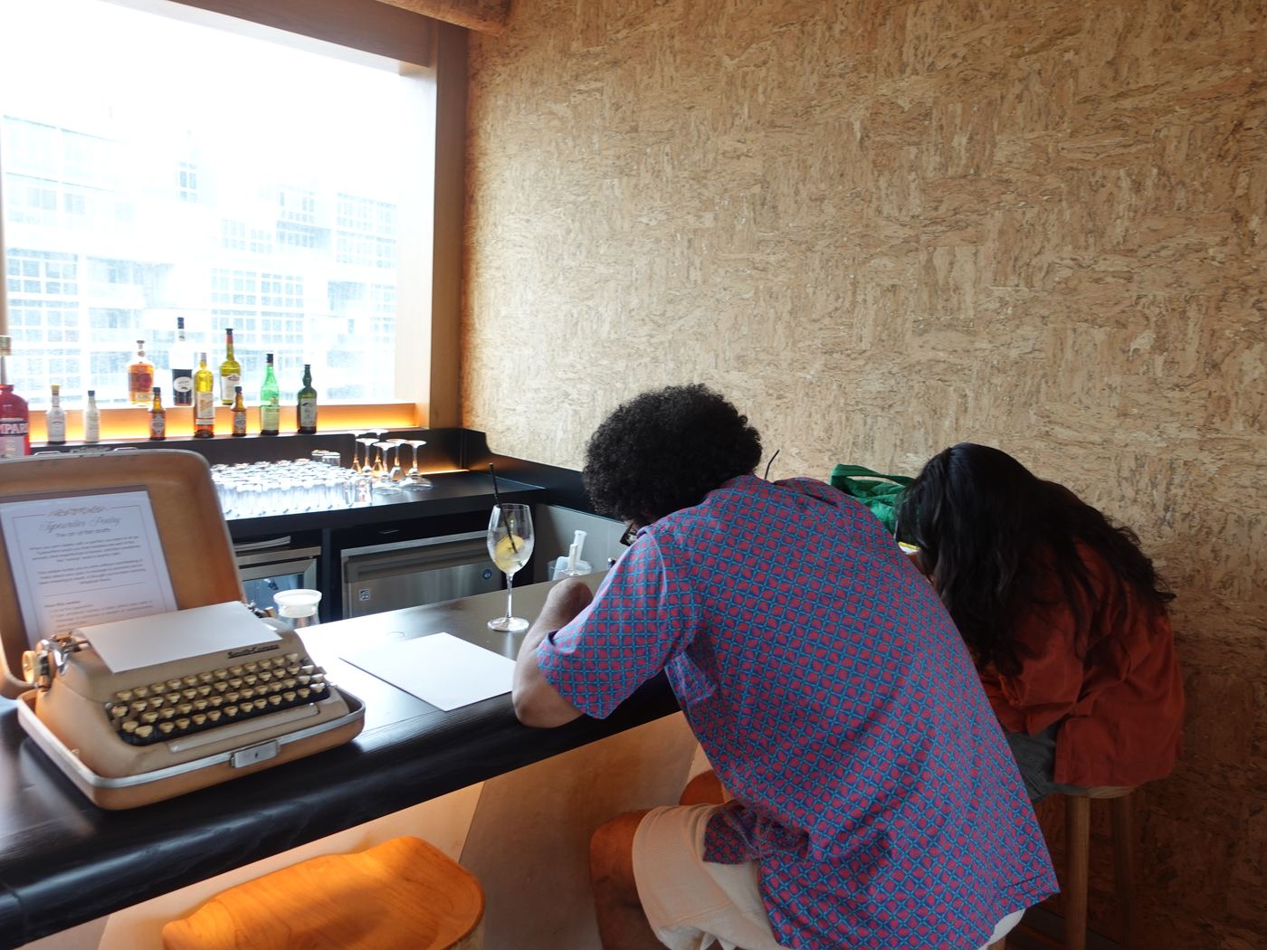 Guests lean over the bar writing, beside a typewriter
