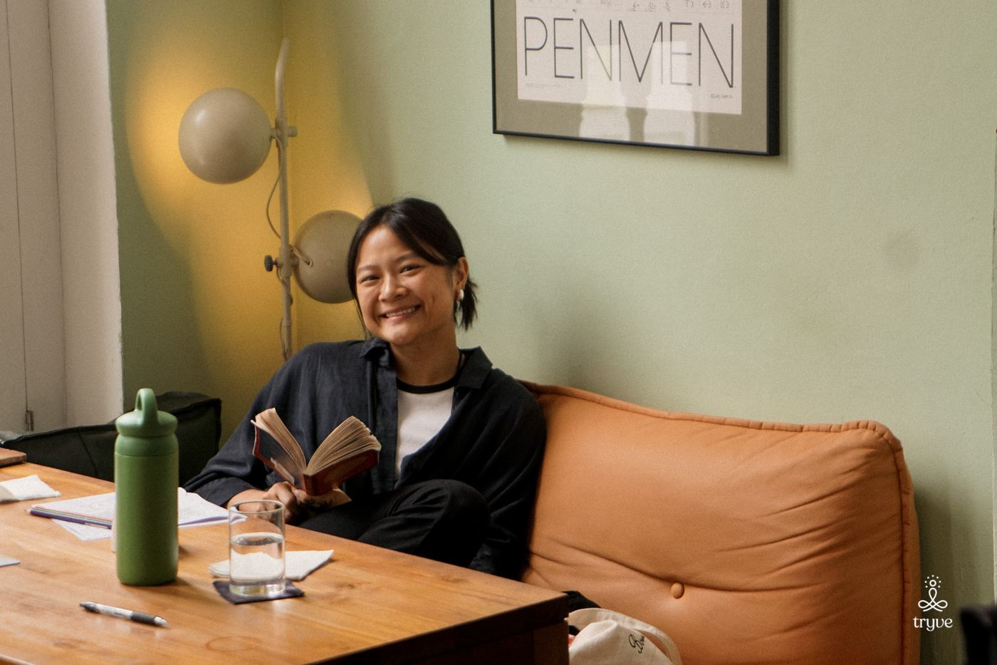 A guest smiles on an orange sofa holding a book